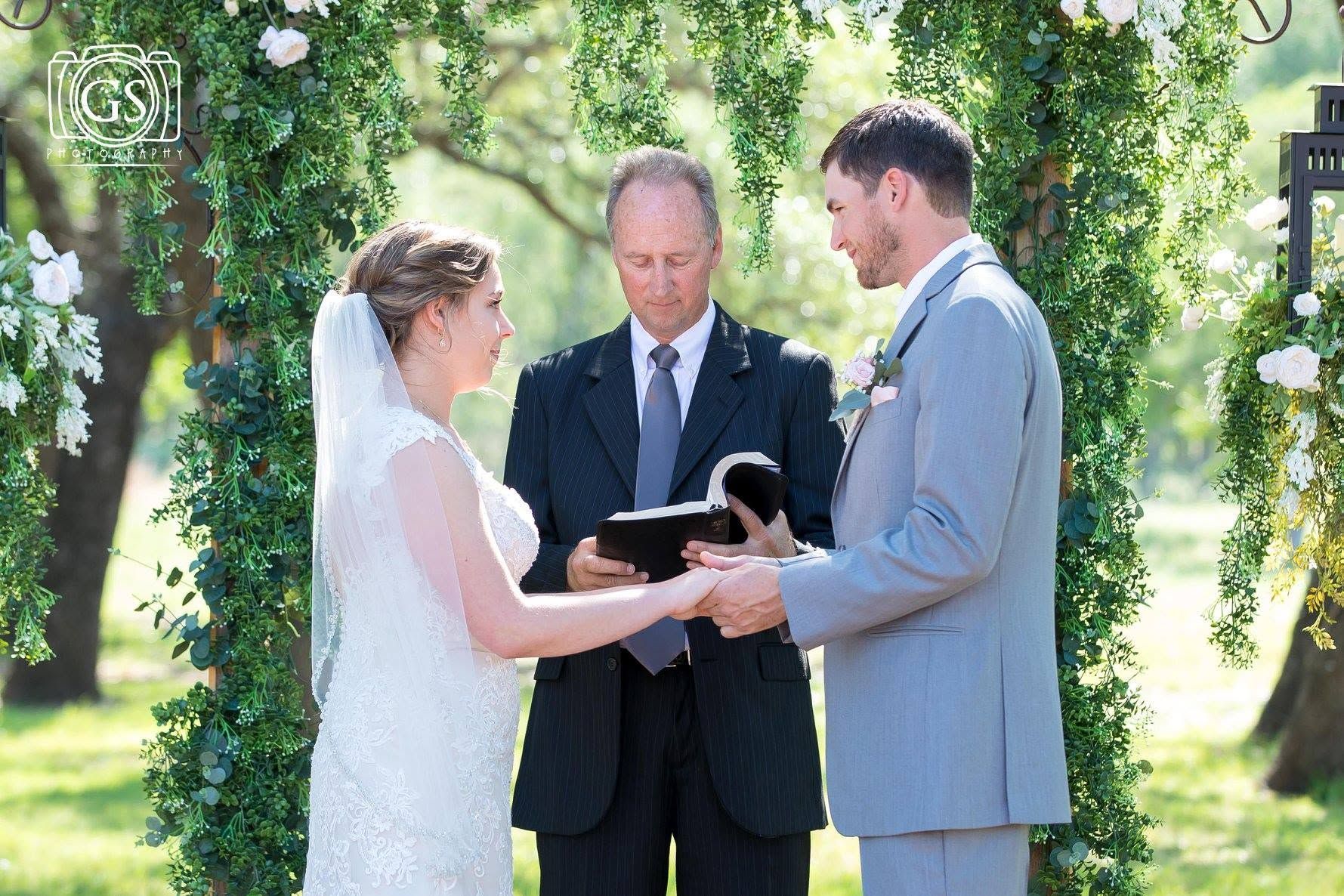 Bride and groom exchanging vows outdoors with officiant holding a book