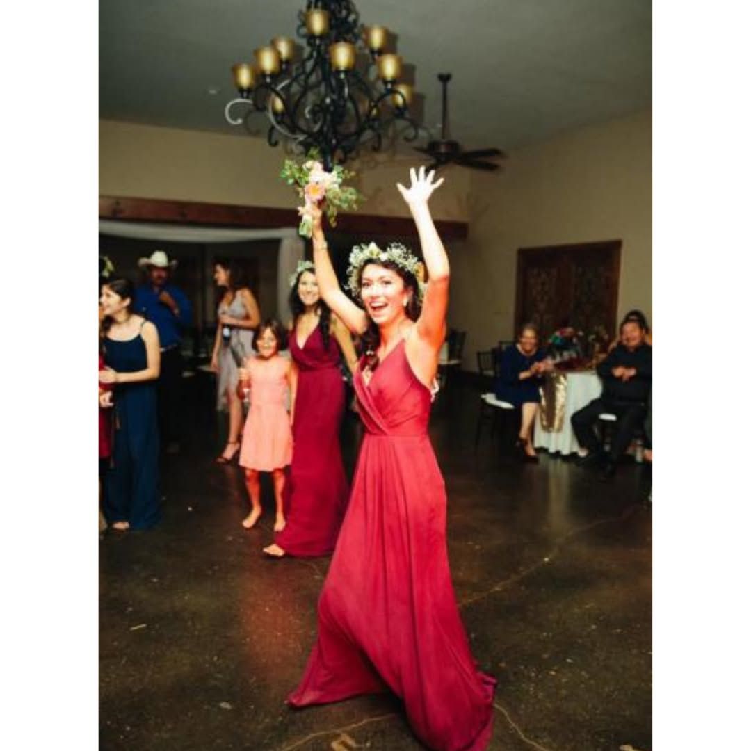 Woman in red dress with arms raised at an indoor celebration, surrounded by guests.
