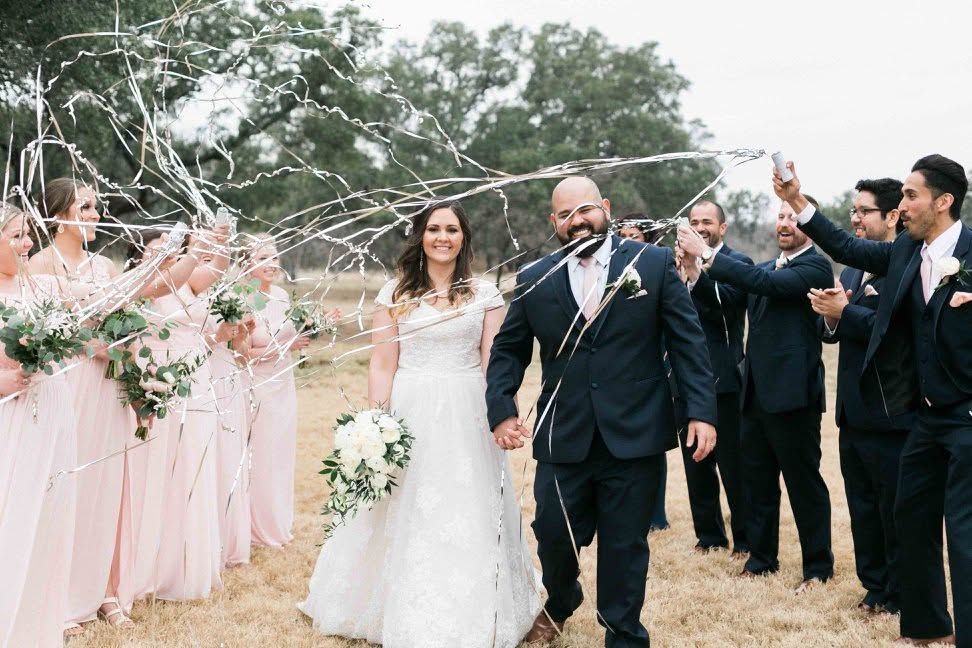 Bride and groom walking down the aisle under a floral arch, smiling outdoors at a wedding ceremony