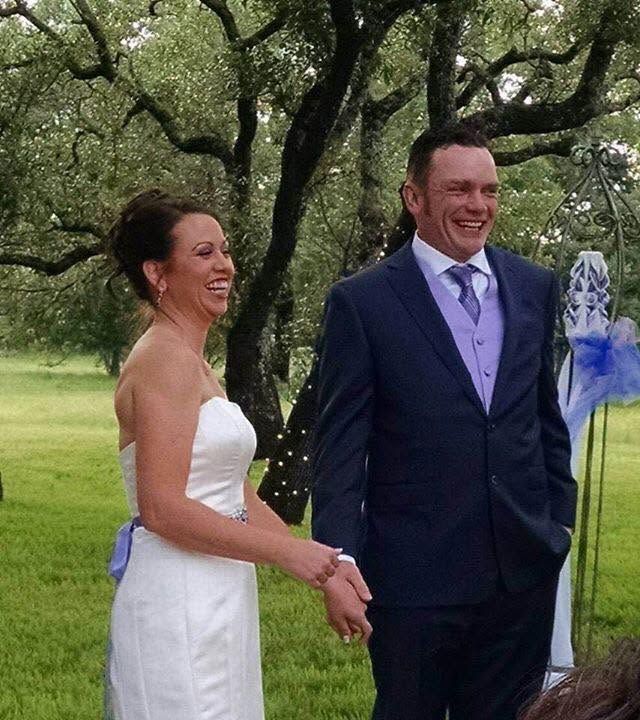Bride and groom smiling outdoors in formal wedding attire under trees