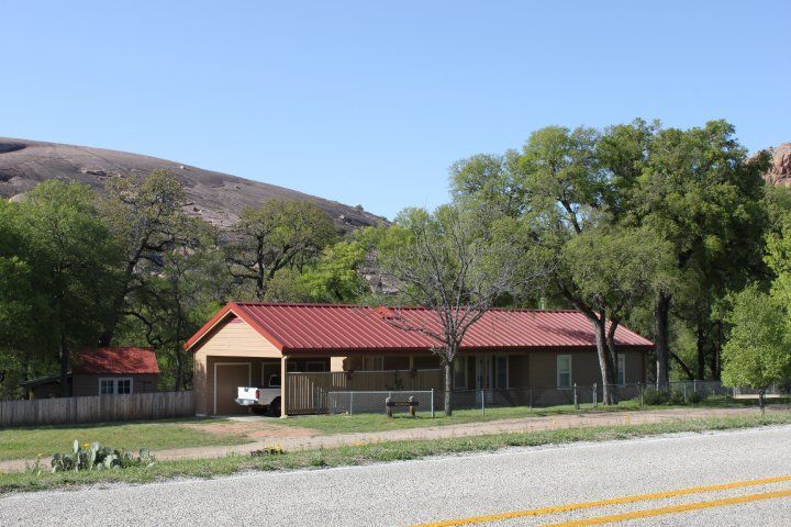 Small tan building with a red roof beside a road, with trees and hills in the background.