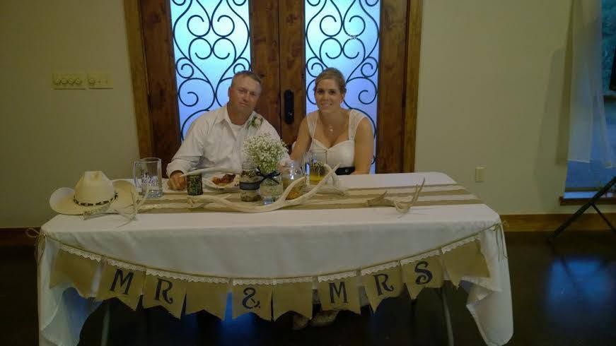 Bride and groom seated at a wedding reception table in front of a stone fireplace