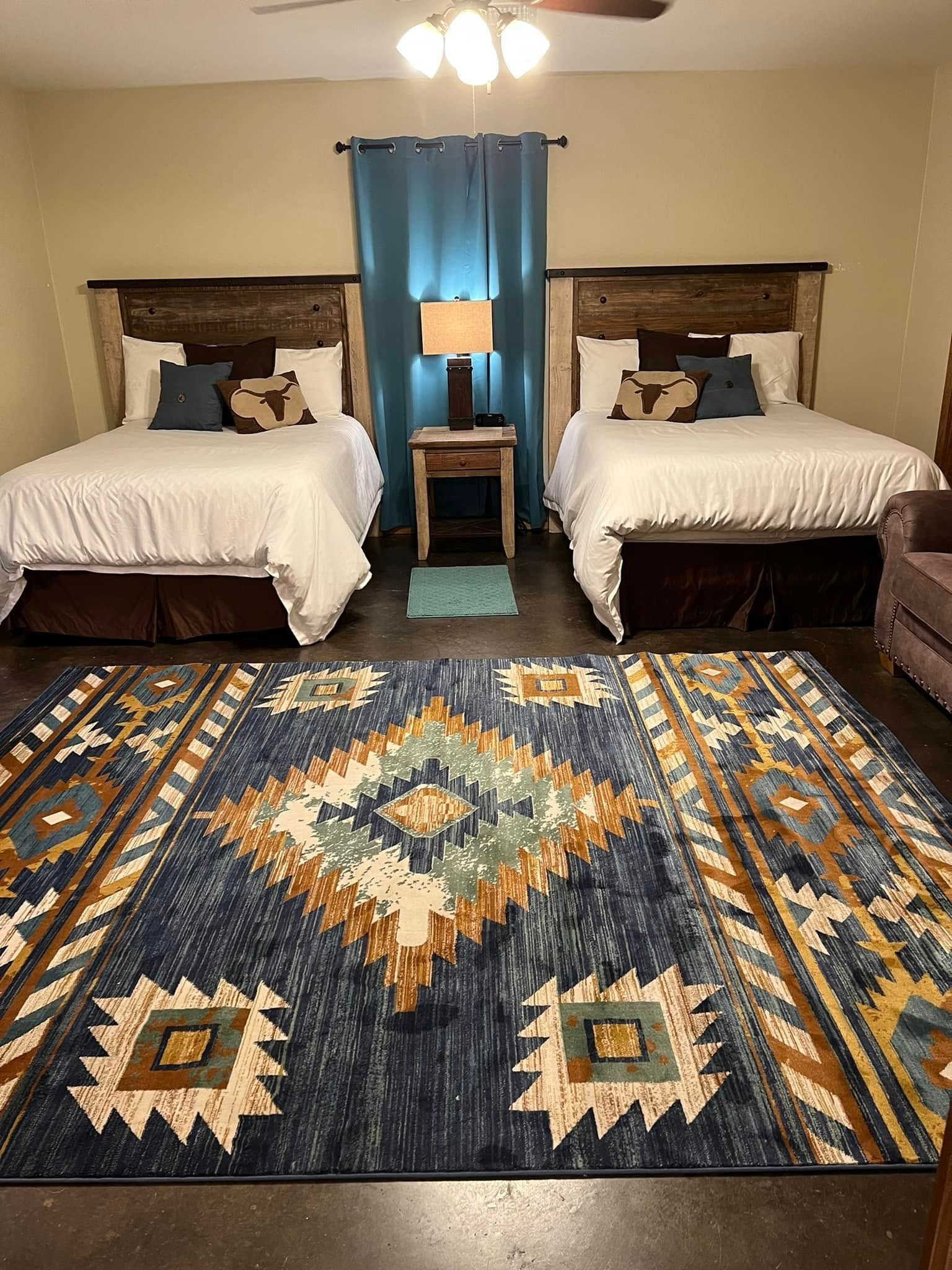 Bedroom with two twin beds, blue curtains, patterned rug, and ceiling fan light