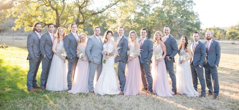 Group of wedding guests in formal attire posing outdoors in front of trees and a lake.