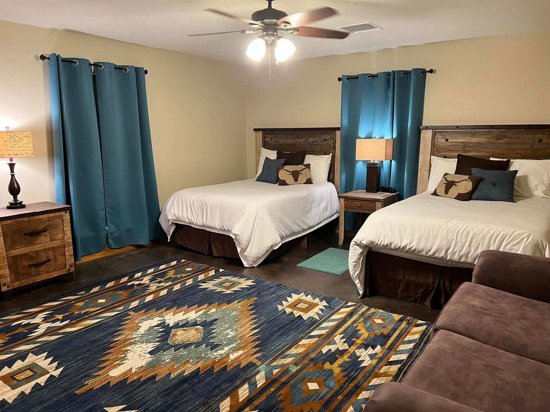 Bedroom with two twin beds, blue curtains, ceiling fan, lamp, and patterned rug