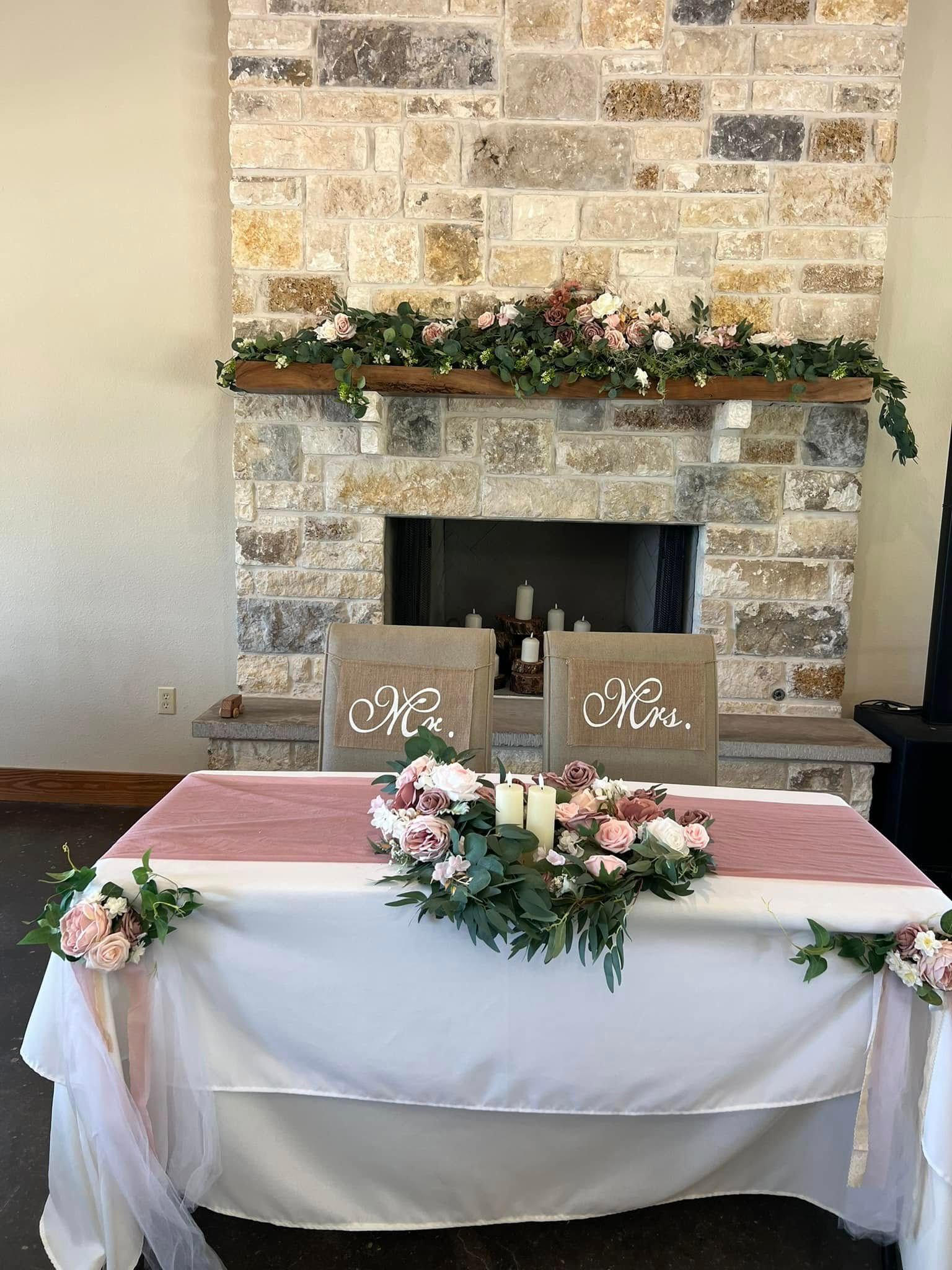 Decorated stone fireplace with mantel, candles, and greenery behind a small round table and two chairs