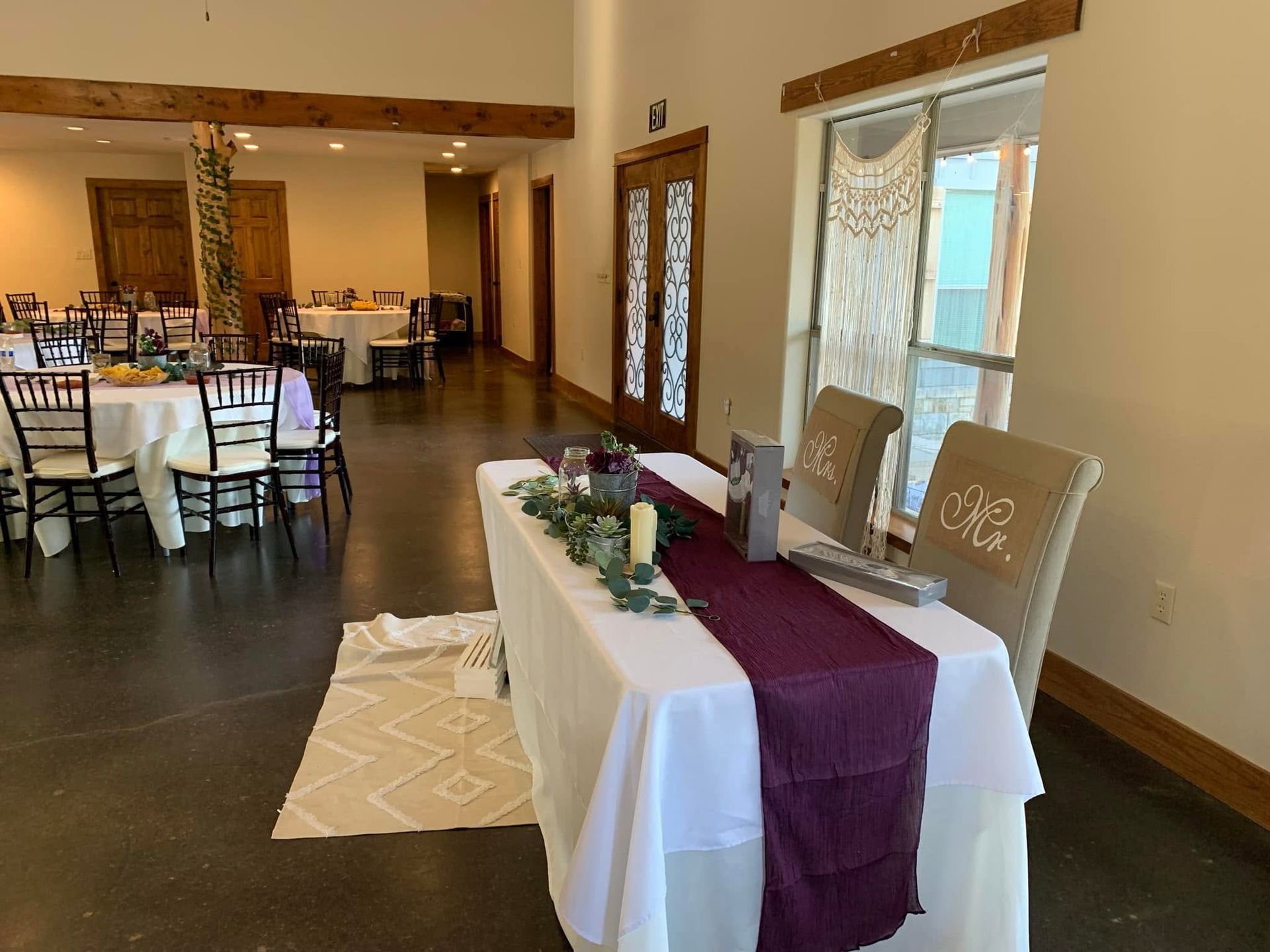 Round dining table set with burgundy runner, greenery centerpiece, folded napkins, and place cards