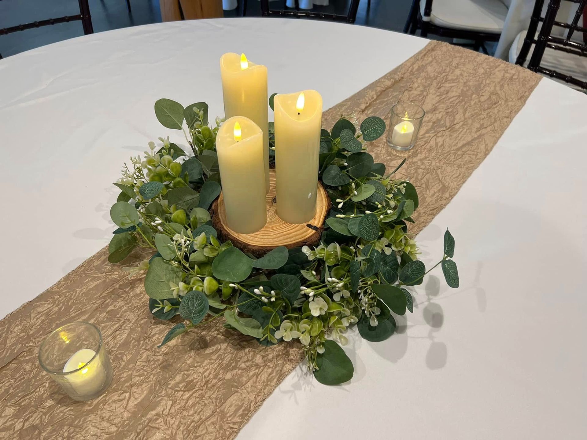 Table centerpiece with cream candles, green foliage, and pink runner on a round banquet table