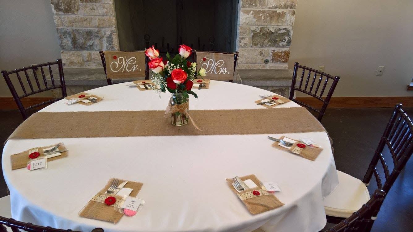 A white-draped table with a red floral arrangement and greenery centerpiece