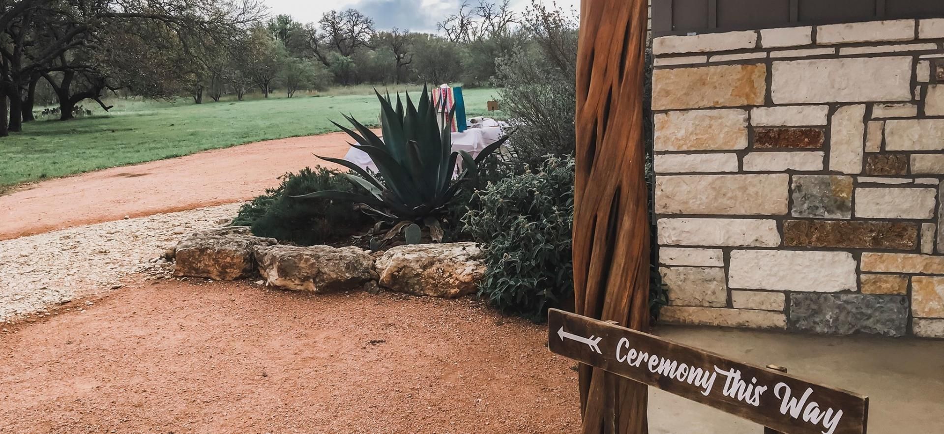Stone wall beside a gravel path and succulent garden with a “Walk Over Here This Way” sign