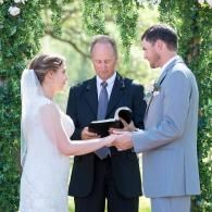 Bride and groom exchanging vows with officiant outdoors under trees