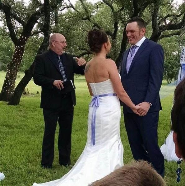 Wedding couple facing each other outdoors, with an officiant nearby in a grassy setting.