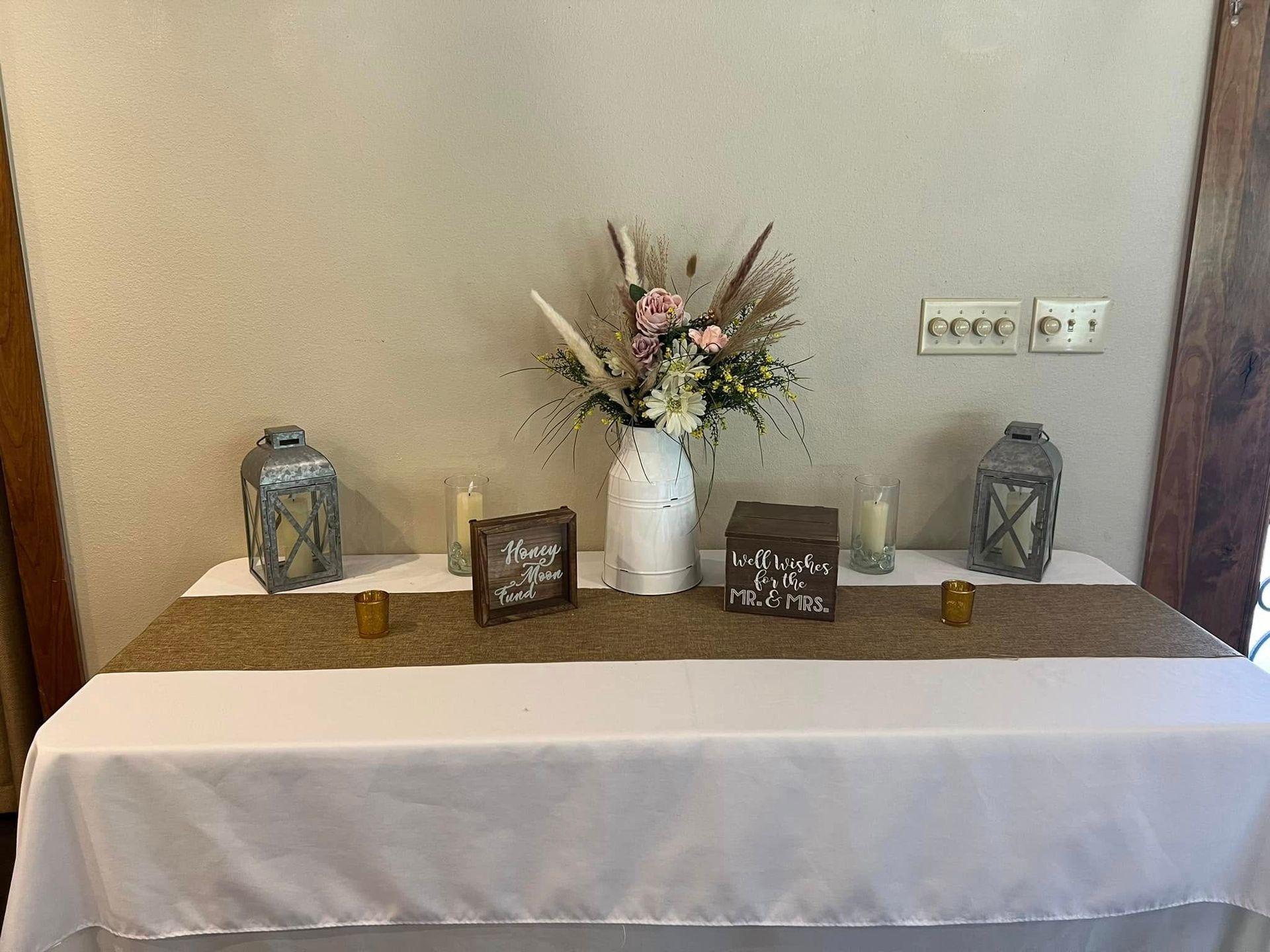 White floral centerpiece with greenery and candles on a table runner in a dining room