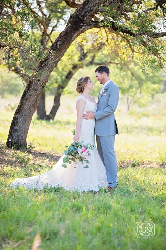 Bride and groom embracing under a tree in a sunlit meadow