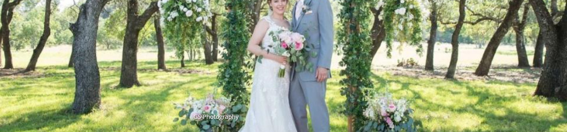 Bride and groom standing together in a sunny garden, holding a pink and white bouquet