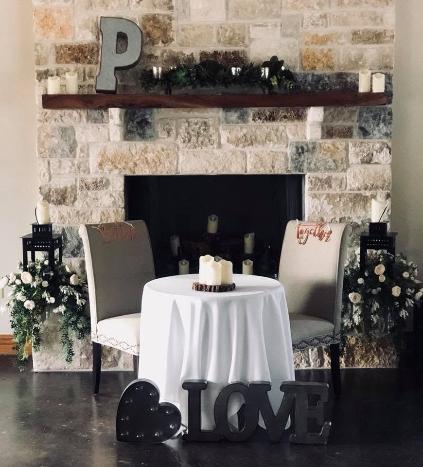 Decorated wedding reception table before a stone fireplace with chairs and floral arrangements
