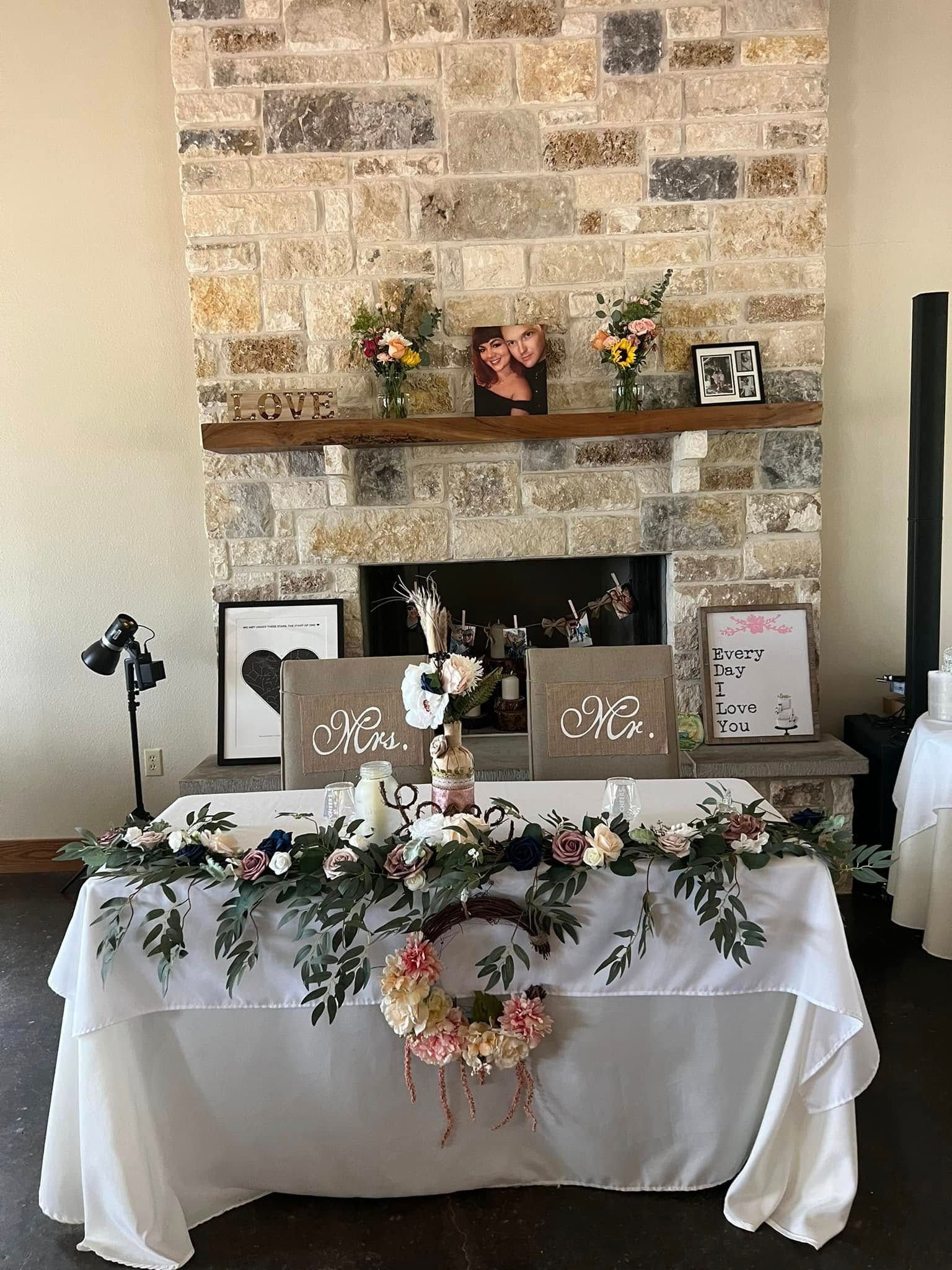 Rustic wedding cake table with white cake, wood sign, and fireplace mantle decorated with greenery