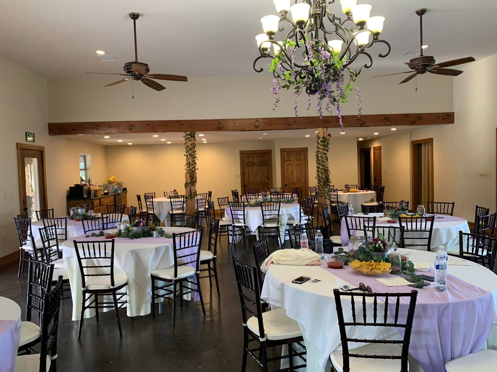 Elegant banquet hall with round tables, black chairs, chandelier, and warm wood accents.