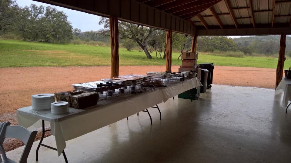 Long serving table under a pavilion with chafing dishes overlooking a grassy outdoor field