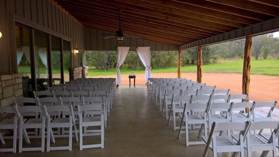 Empty outdoor pavilion with rows of white chairs facing a small table and draped backdrop.