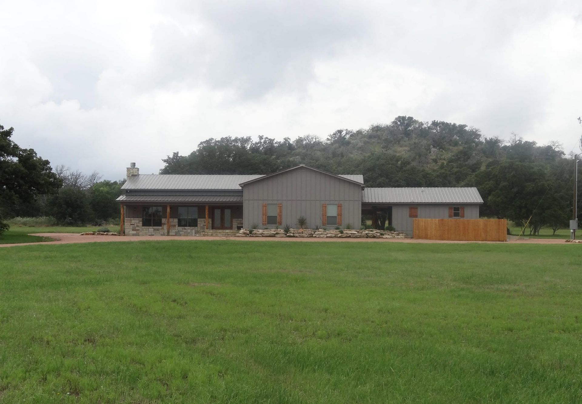 Single-story gray house with a dark roof and large front lawn under an overcast sky