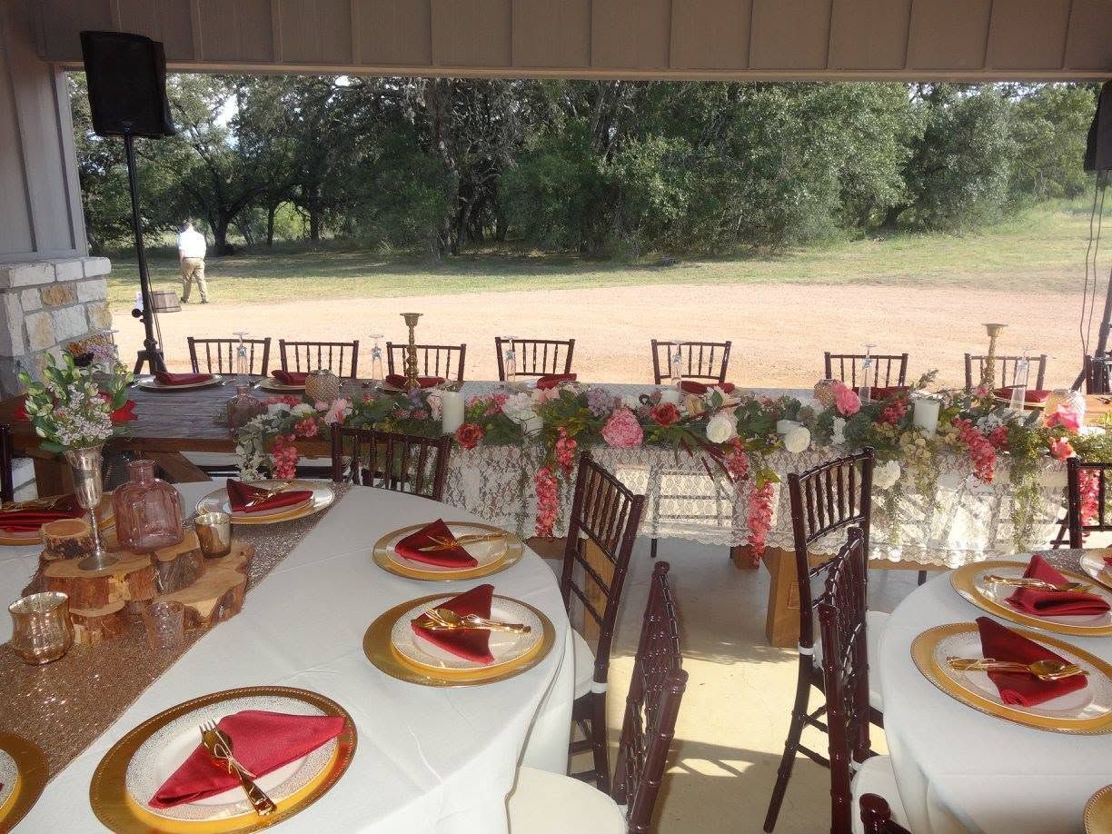 Outdoor banquet setup with round tables, white tablecloths, and red napkins under a shaded canopy