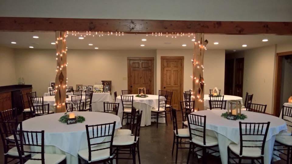 Empty banquet hall with round tables and black chairs, dark floors, ceiling fans, and double glass doors