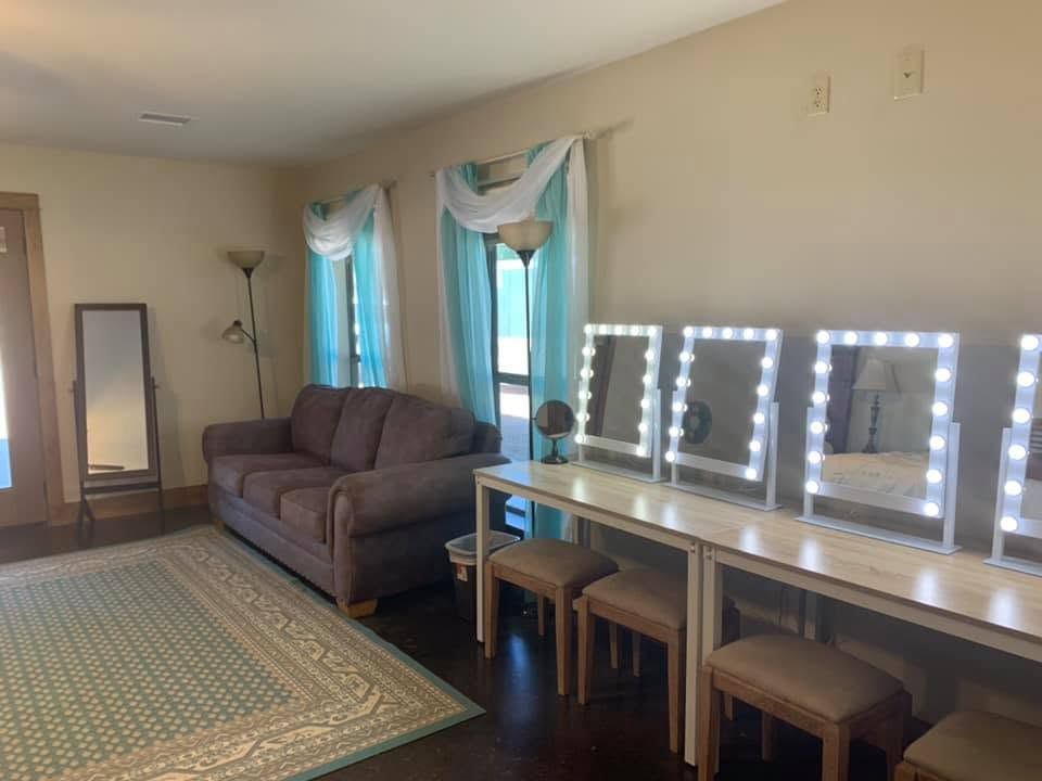 Living room with gray sofa, rug, draped blue curtains, and a vanity table with lit mirrors and stools