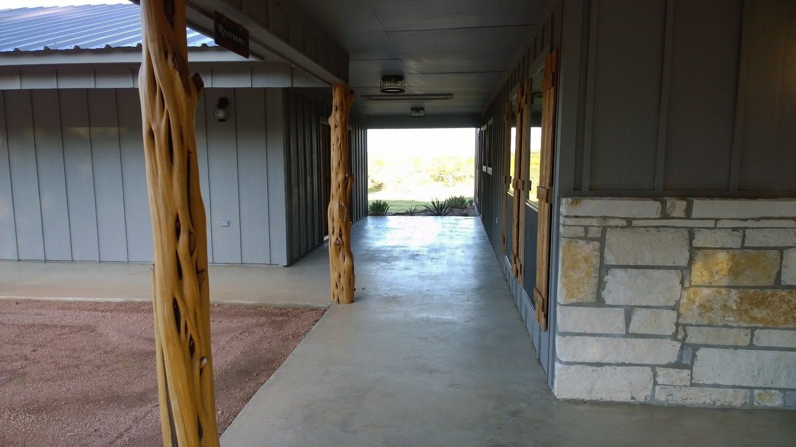 Covered porch with wooden shutters, concrete floor, and rustic log posts overlooking a grassy yard