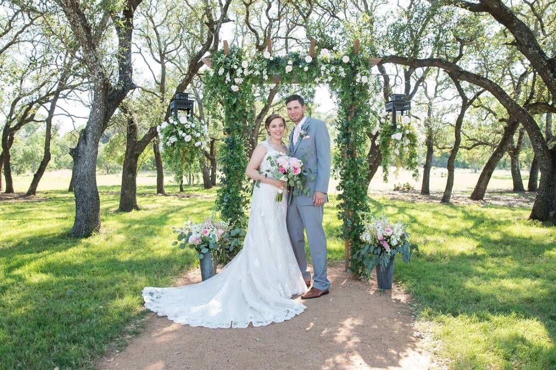 Bride and groom posing outdoors in a sunlit garden with trees and flowers