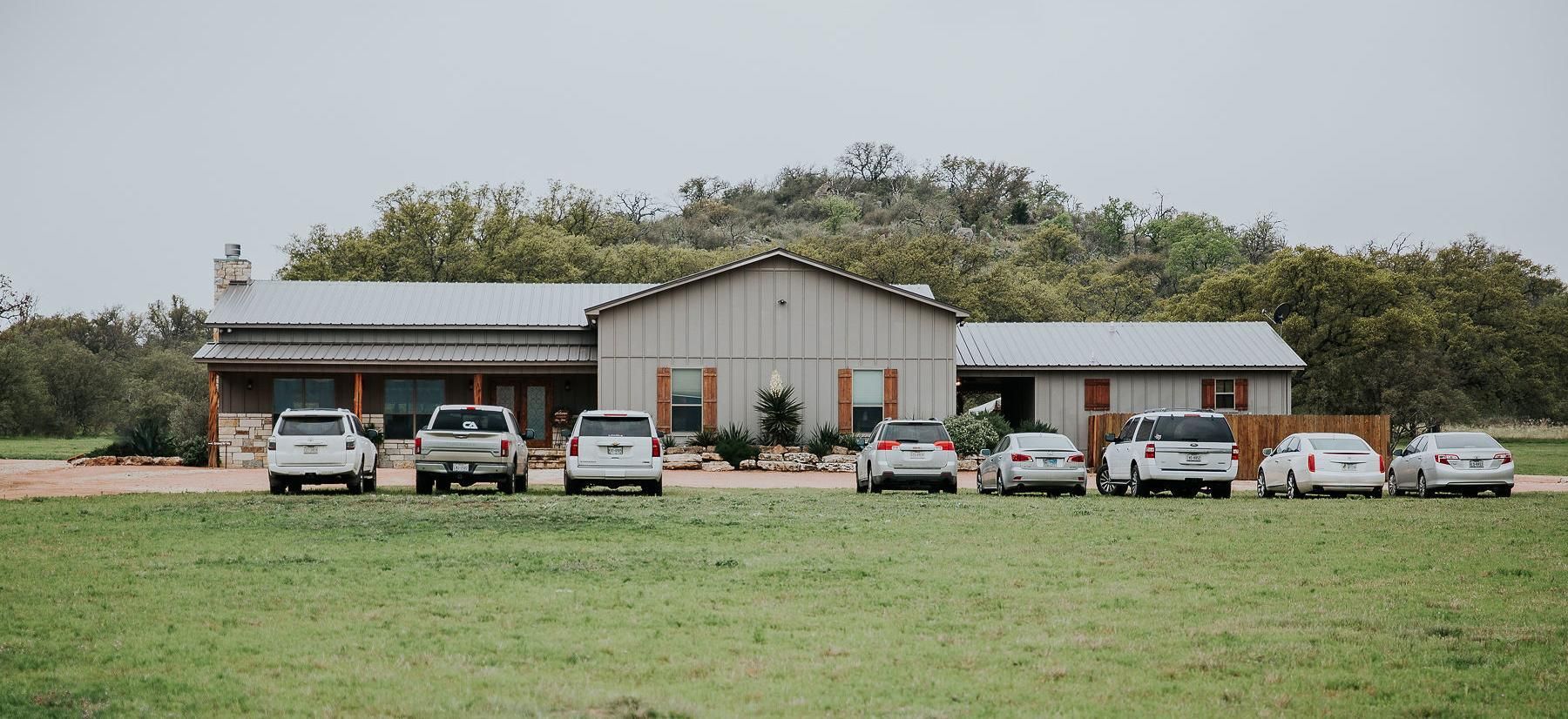 Single-story building with a metal roof and several cars parked in front on a grassy lot