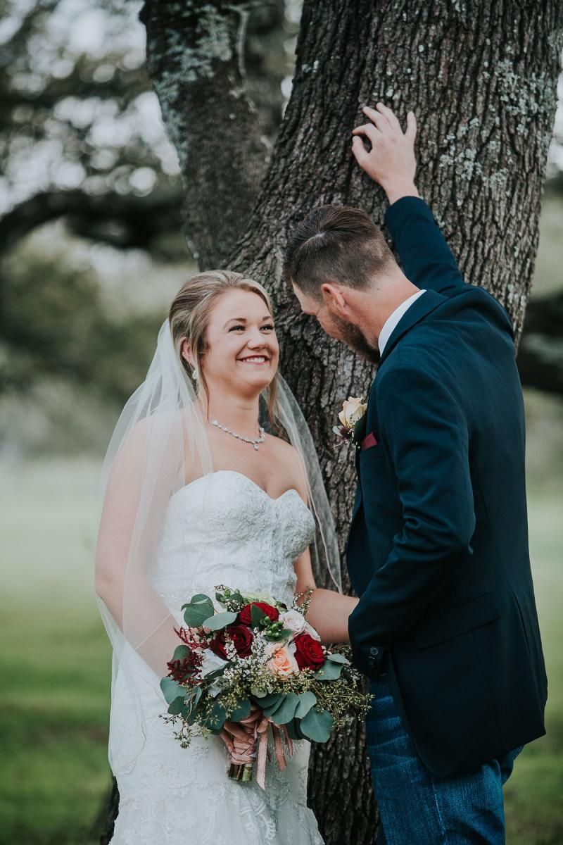 Bride and groom sharing a moment beside a tree, with the bride holding a bouquet.