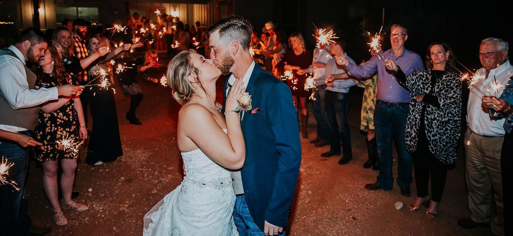 Bride and groom kissing at a candlelit reception while guests applaud and dance around them