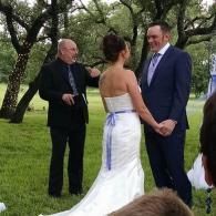 Bride in a white gown and man in a navy suit holding hands outdoors at a wedding ceremony.