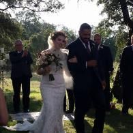 Bride in white lace dress and groom in dark suit walking outdoors at a wedding ceremony