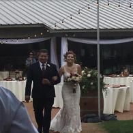 Bride and groom walking outdoors at a wedding reception, with tables and a tent in the background