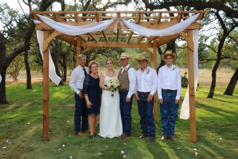 Wedding party posing under a wooden arch outdoors in a grassy field