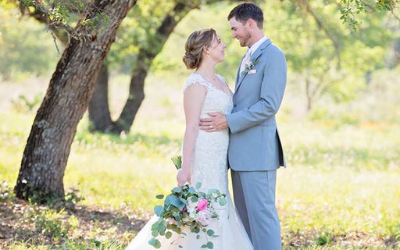 Bride and groom embracing outdoors under a tree, with a bouquet at the bride’s side