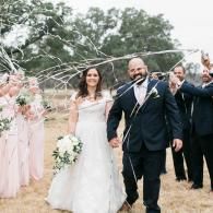 Bride and groom walking hand in hand through a wedding arch as guests celebrate nearby