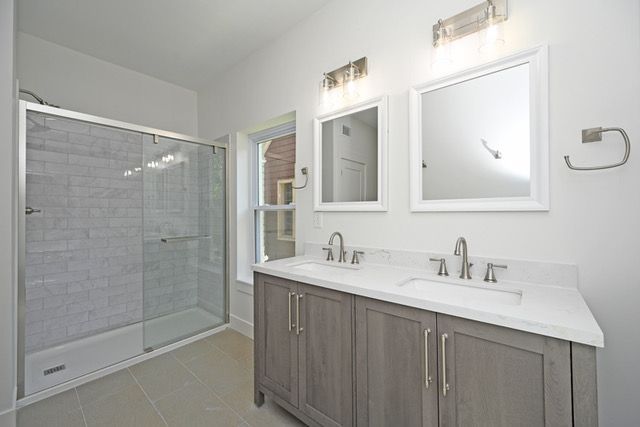 A bathroom with two sinks , two mirrors and a walk in shower.