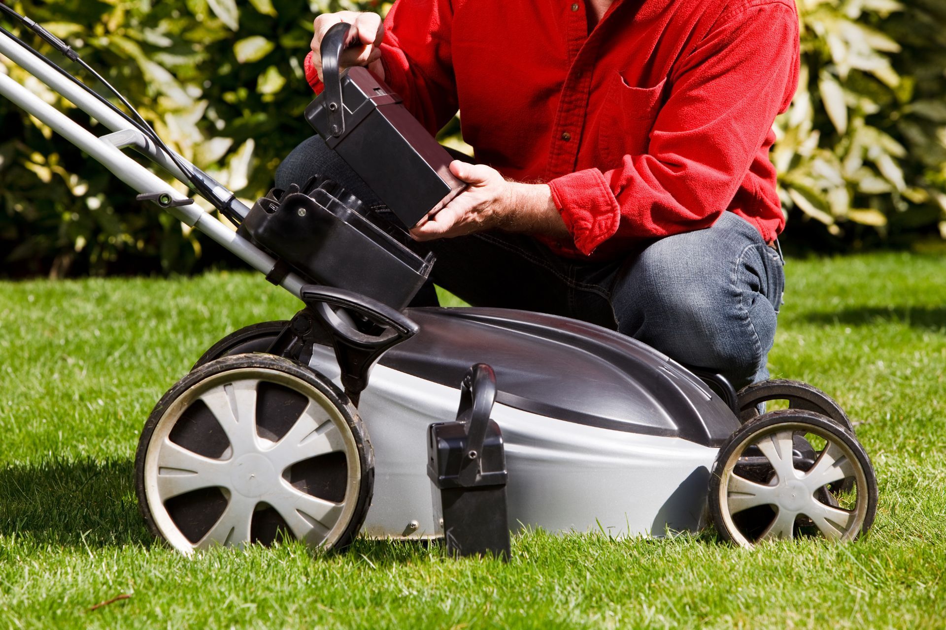 Man inserts battery into eco-friendly lawn mower in Athens garden.