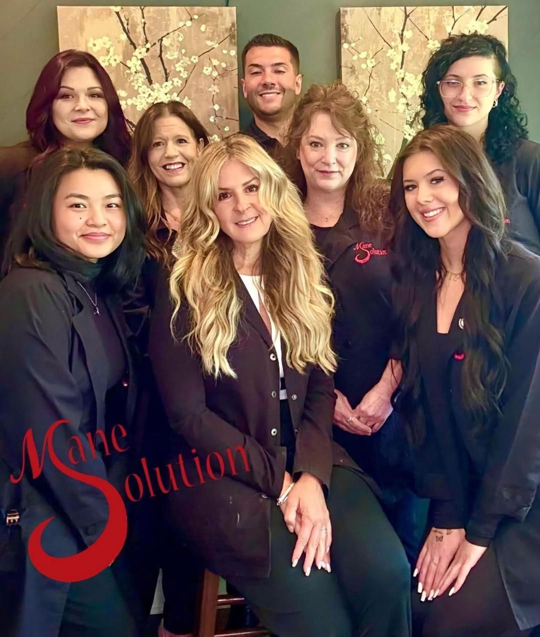 A group of people are posing for a picture and one of them is sitting on a stool.