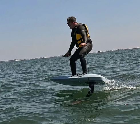 Person riding a hydrofoil board over choppy water under a clear sky
