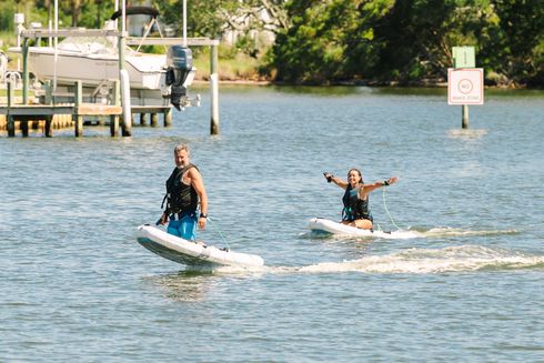 Two people riding jet skis on a lake, with a dock and trees in the background.