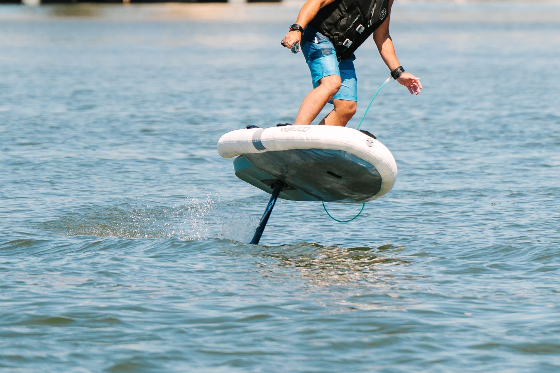 Person riding a hydrofoil board over calm blue water, balancing above the surface