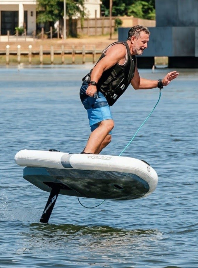 Man riding a foil board on calm water, holding a handle attached to a line.