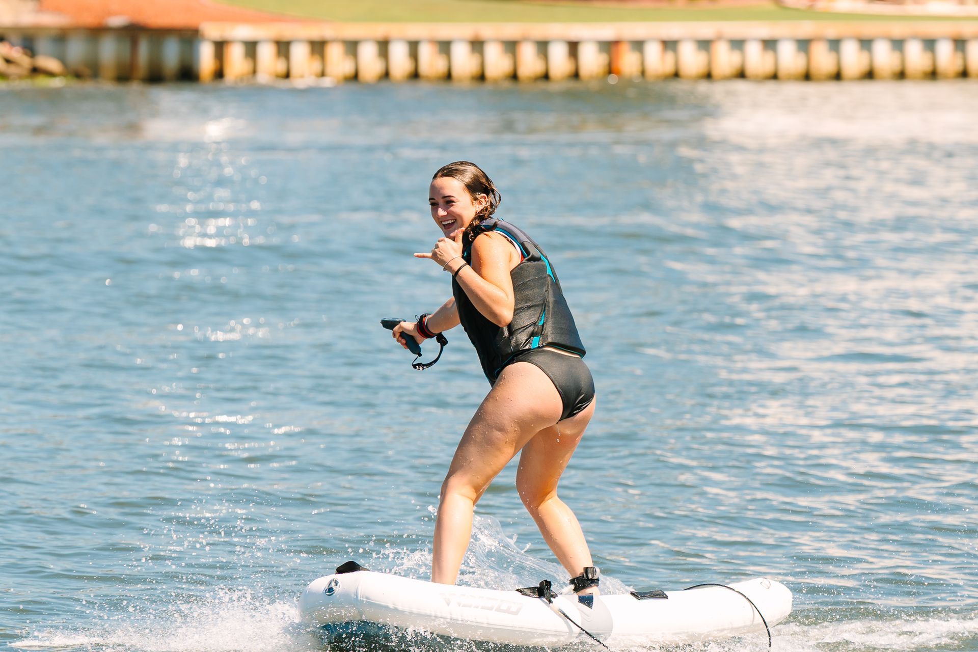 Person eFoiling on blue water, holding a handle and smiling near a dock.