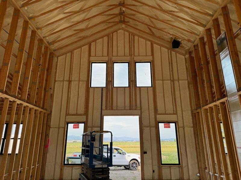 Spray foam insulation being applied to wooden rafters in an attic.