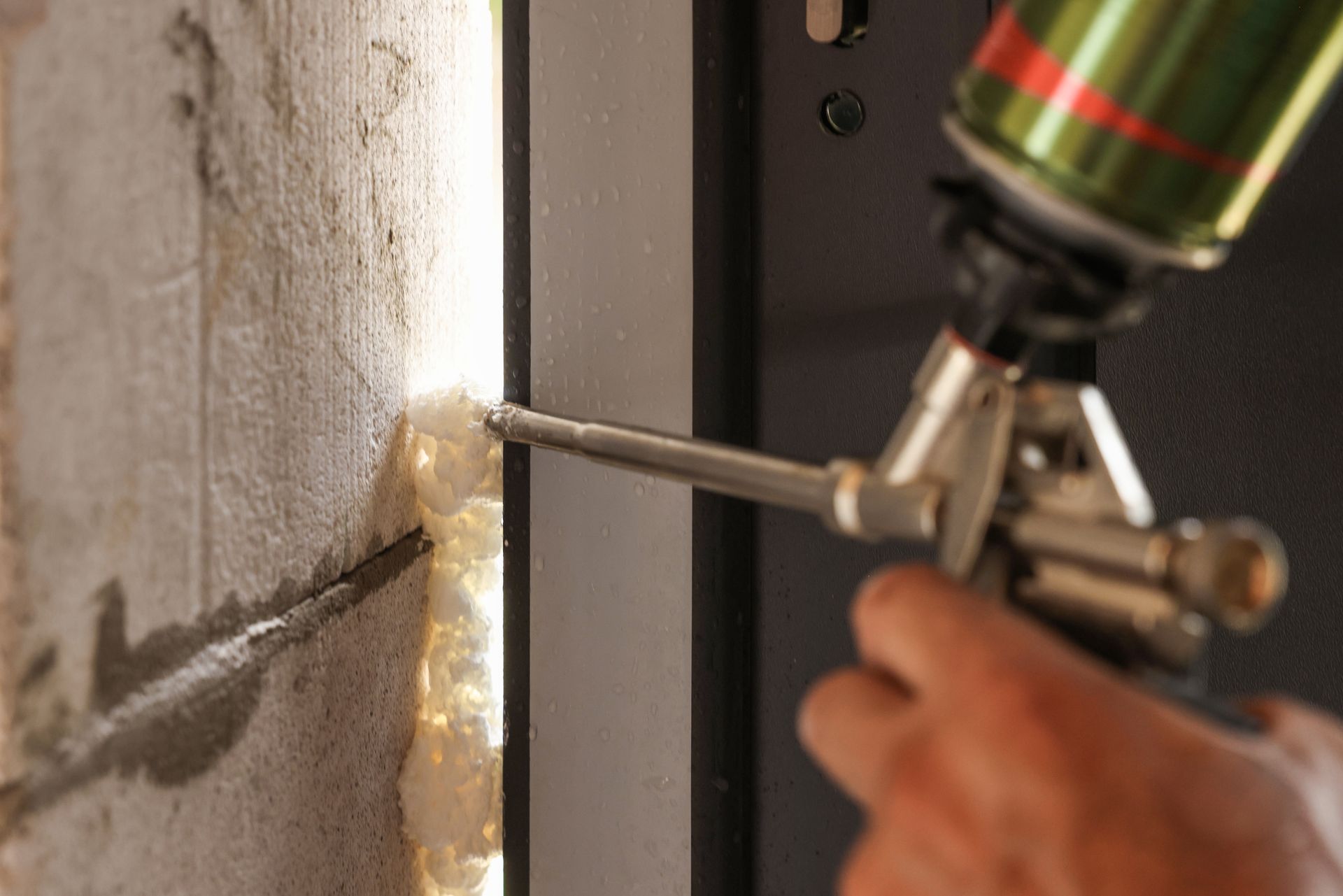 A person using spray foam to seal a gap between a concrete wall and a metal door frame.