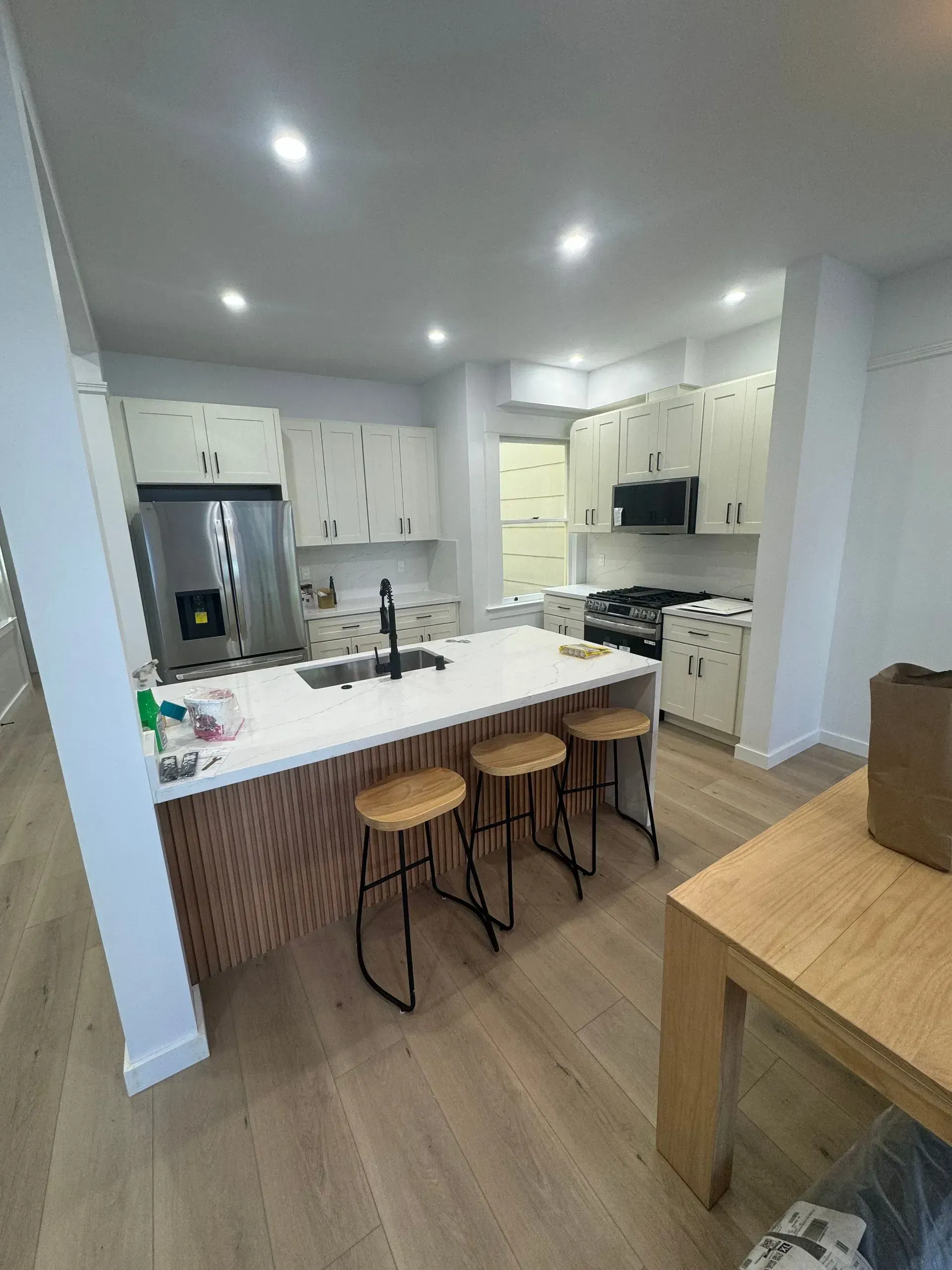 A kitchen with a large island , stools , a table and a refrigerator.